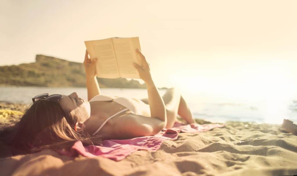 a lady reading book while tanning in the morning