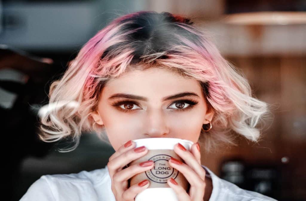 lady with a pink hair is drinking a coffee