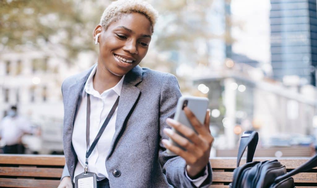 a vey short hair woman on a business suit using her cellphone on a bench