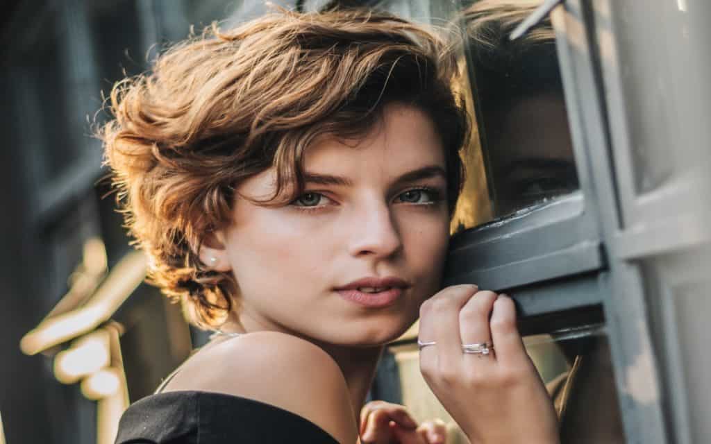 a beautiful woman with curly short hair posing beside a window