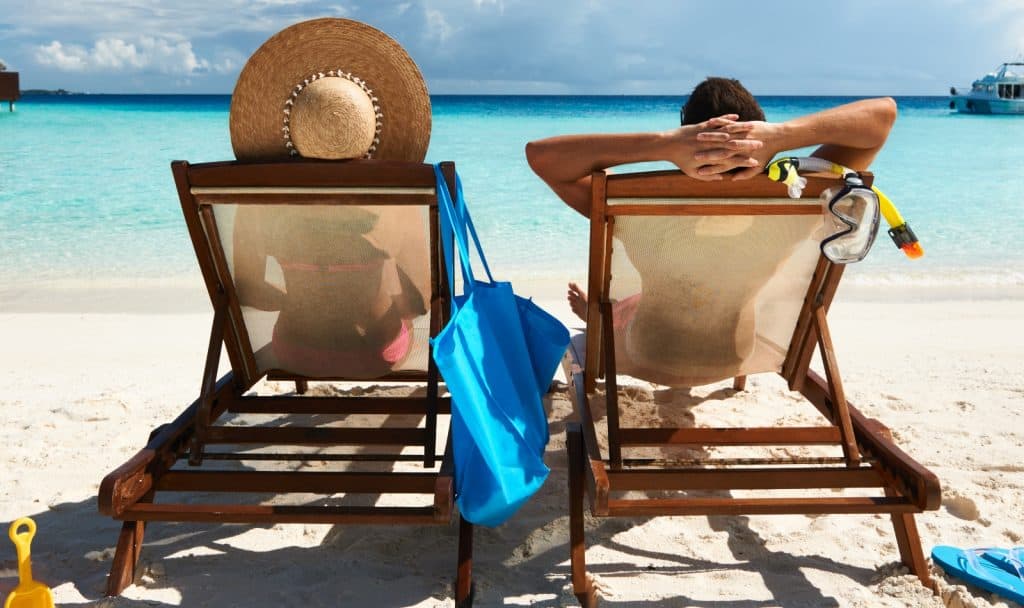 couple sitting on a beach chair while tanning