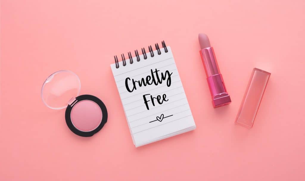 Cruelty free text on notebook with lipstick and blush on pink background, flat lay