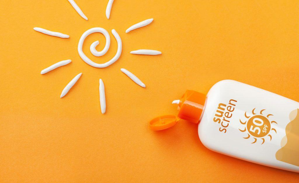 Sunscreen on orange background. Plastic bottle of sun protection and white sun-shaped cream.