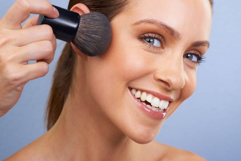 a smiling pretty lady showing how to apply bronzer to contour