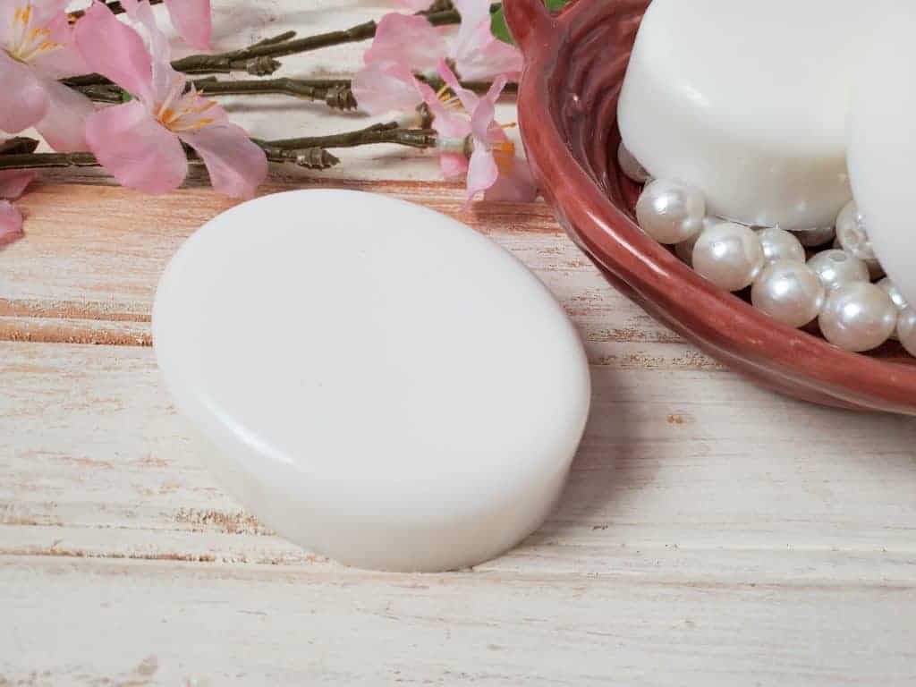 homemade coconut shampoo bar on a wooden background with pearls and pink flowers