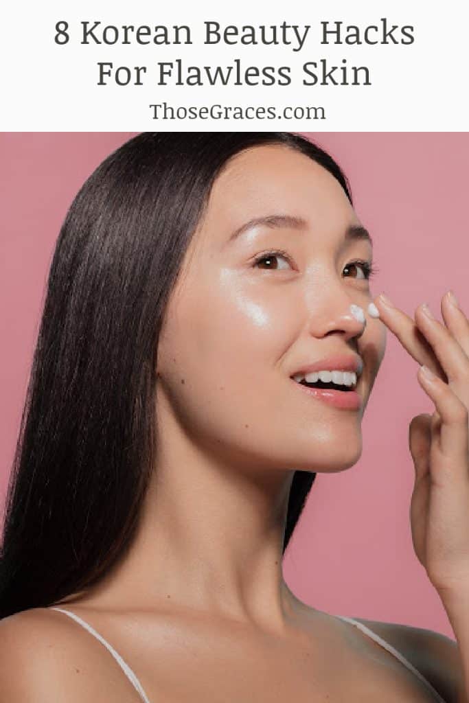 Korean woman applying skincare cream to her nose with a pink background behind her. 