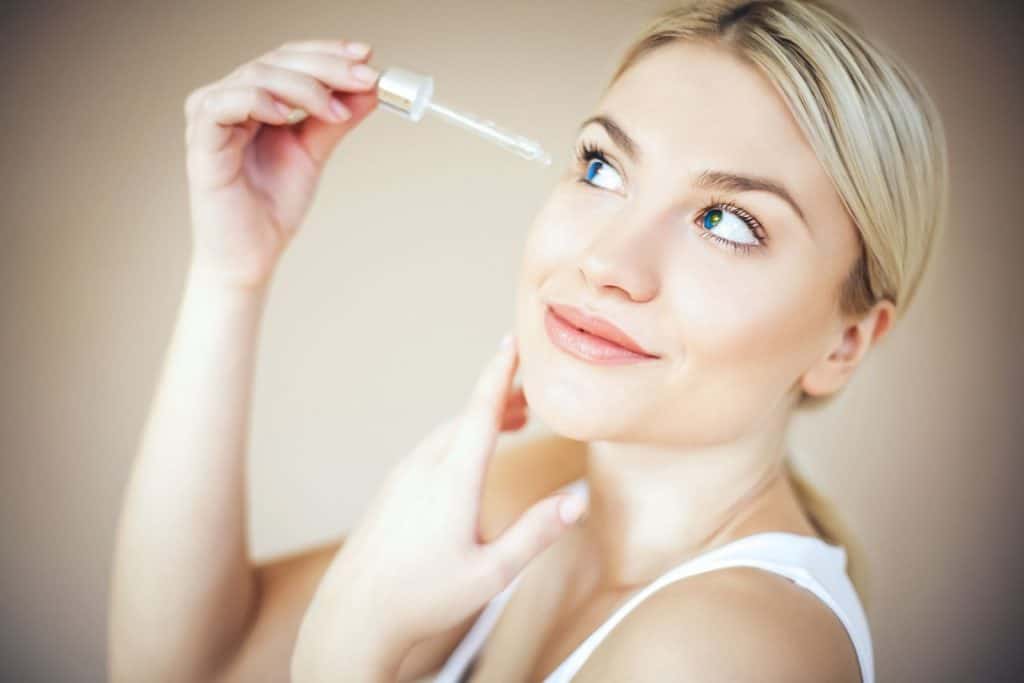 blonde woman putting eyelash serum on her lashes