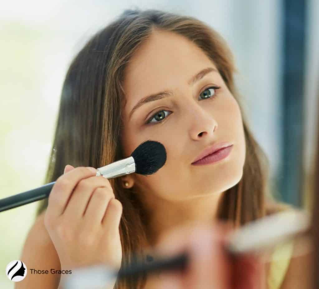 a pretty woman blending the makeup primer on her face using a brush