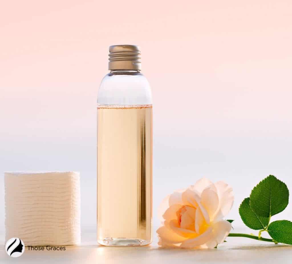 essence in a bottle with rose and cotton pads beside it